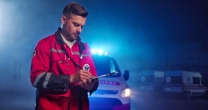 Male EMS professional writing on a clipboard in front of an ambulance